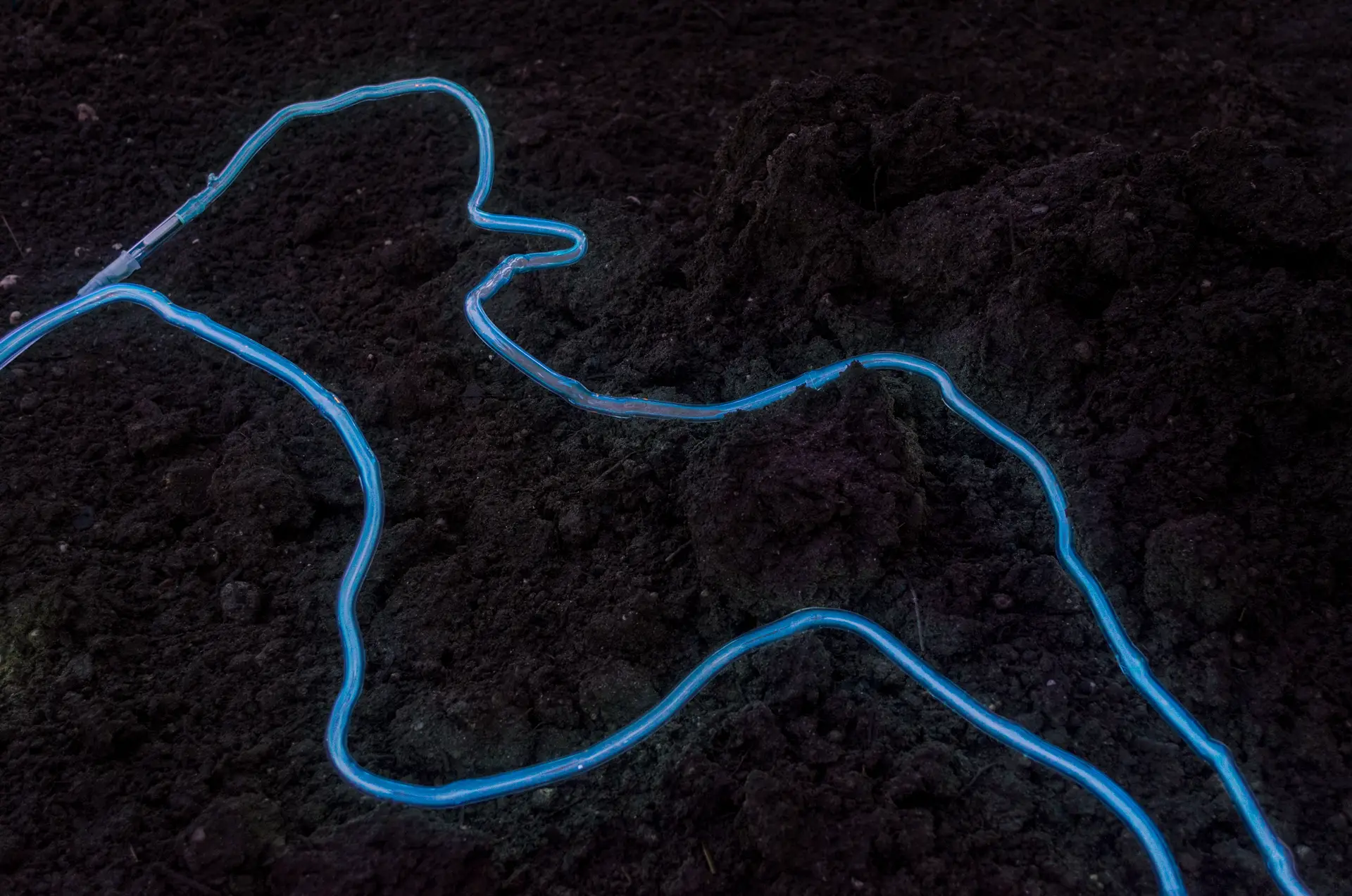 Deux néons bleus reposent sur un sol de terre sombre, vue de l'installation Candela (2022).