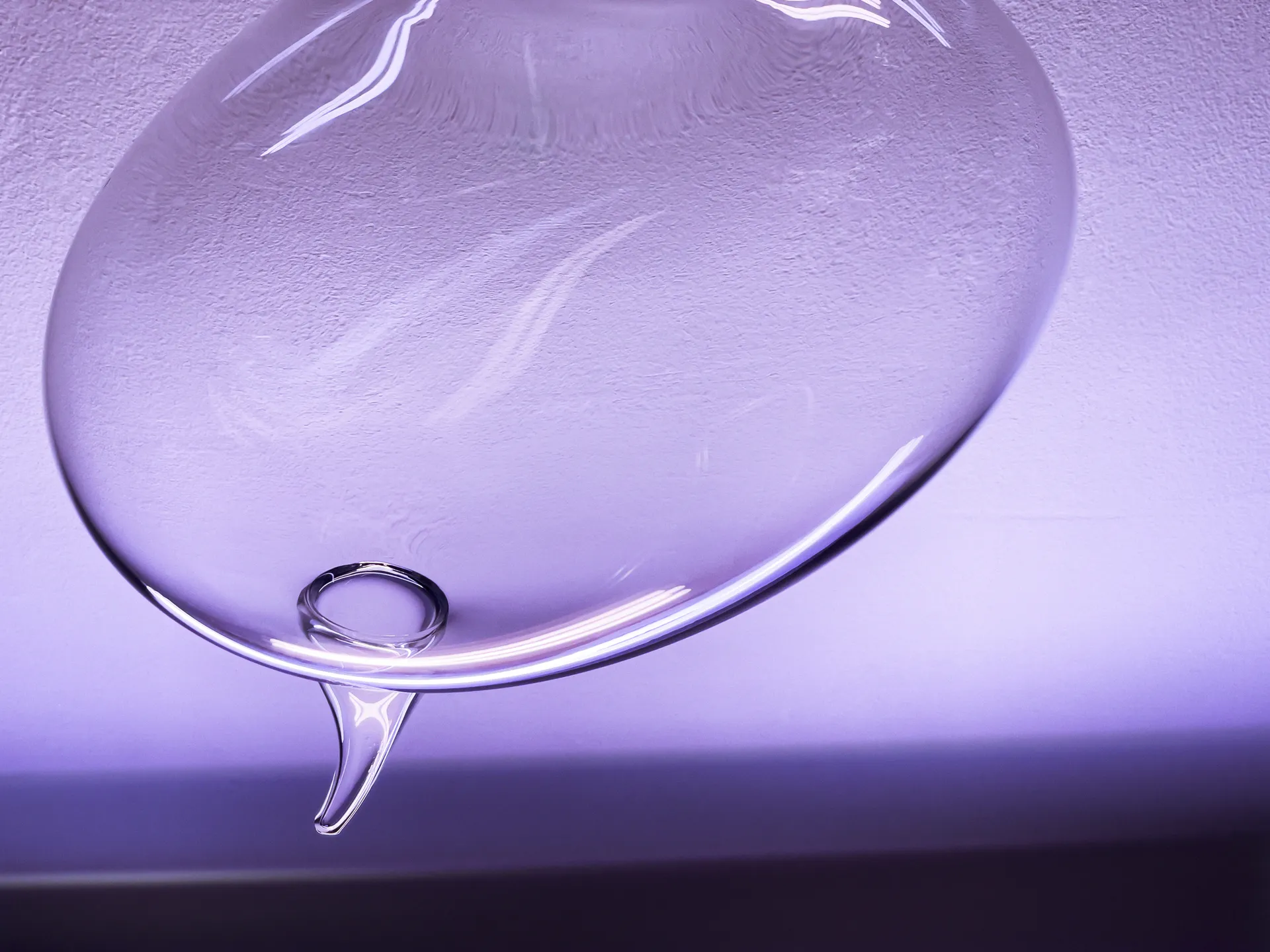 Un phylactère en verre transparent est suspendu dans une lumière mauve, détail de l'installation Formules (2022).
